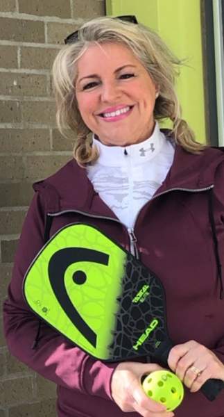 Woman smiling while holding a pickleball paddle and ball