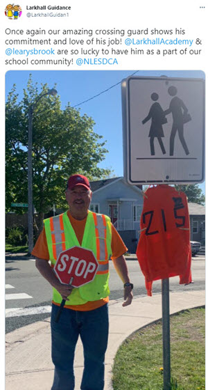 a crossing guard holding a stop sign and standing next to an orange shirt with the number 215 on it to represent the number of graves found (at that time) near Canadian residential schools