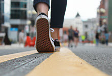 Image of the road showing a yellow line with a person walking away showing the bottom of the sneakers.