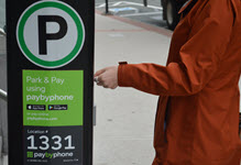 Image of a person wearing an orange coat, using a pay station. The signage on the pay station is green and white, with a large letter 'P' in a green circle.
