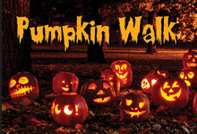 Several pumpkins are carved and illuminated on the ground at a park. Orange text at the top of the image says 'Pumpkin Walk'.