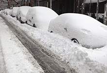 Image of vehicles parked on the street covered in snow.