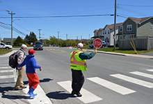 Crossing Guard holding up STOP sign while on crosswalk to guide a father and son across