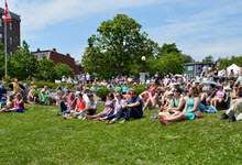 A Crowd of people sitting on the grass watching a concert at Harbourside Park.