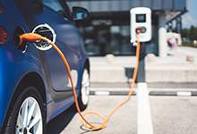 a blue electric vehicle plugged into a charging station with an orange hose