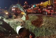 Excavator installing underground pipe at night