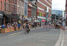 Image taken on Water Street during the summer showing outdoor patios with patrons and a person on a bike.
