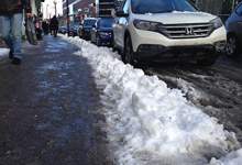 Image of a sidewalk with snow on the side of the road and cars parked.
