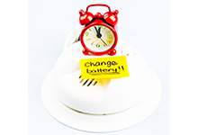 a smoke detector with a red alarm clock on top of it and a yellow note on it with text: change batteries!